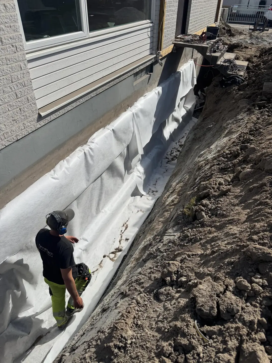 Dräneringsarbete med markduk längs en husgrund
